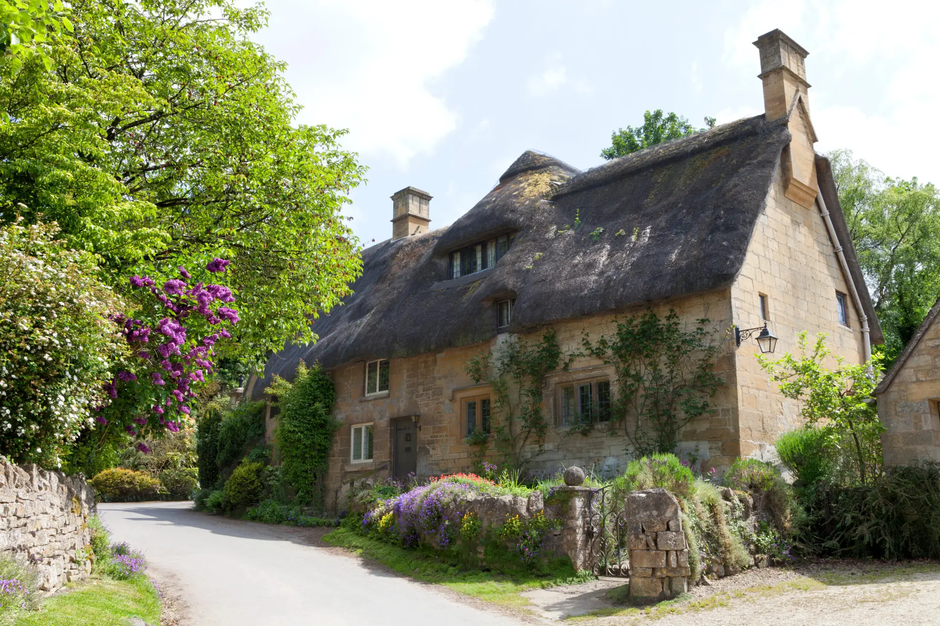 Thatched roof, stone cottage with flowering gardens,  by a country road, on a summer sunny day .