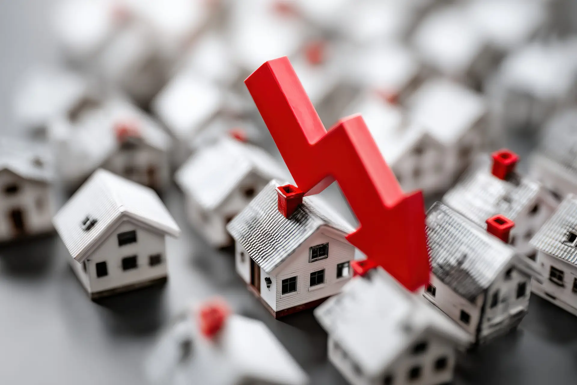 Cluster of small homes beneath a large red arrow pointing down, symbolizing housing crash or real estate decline