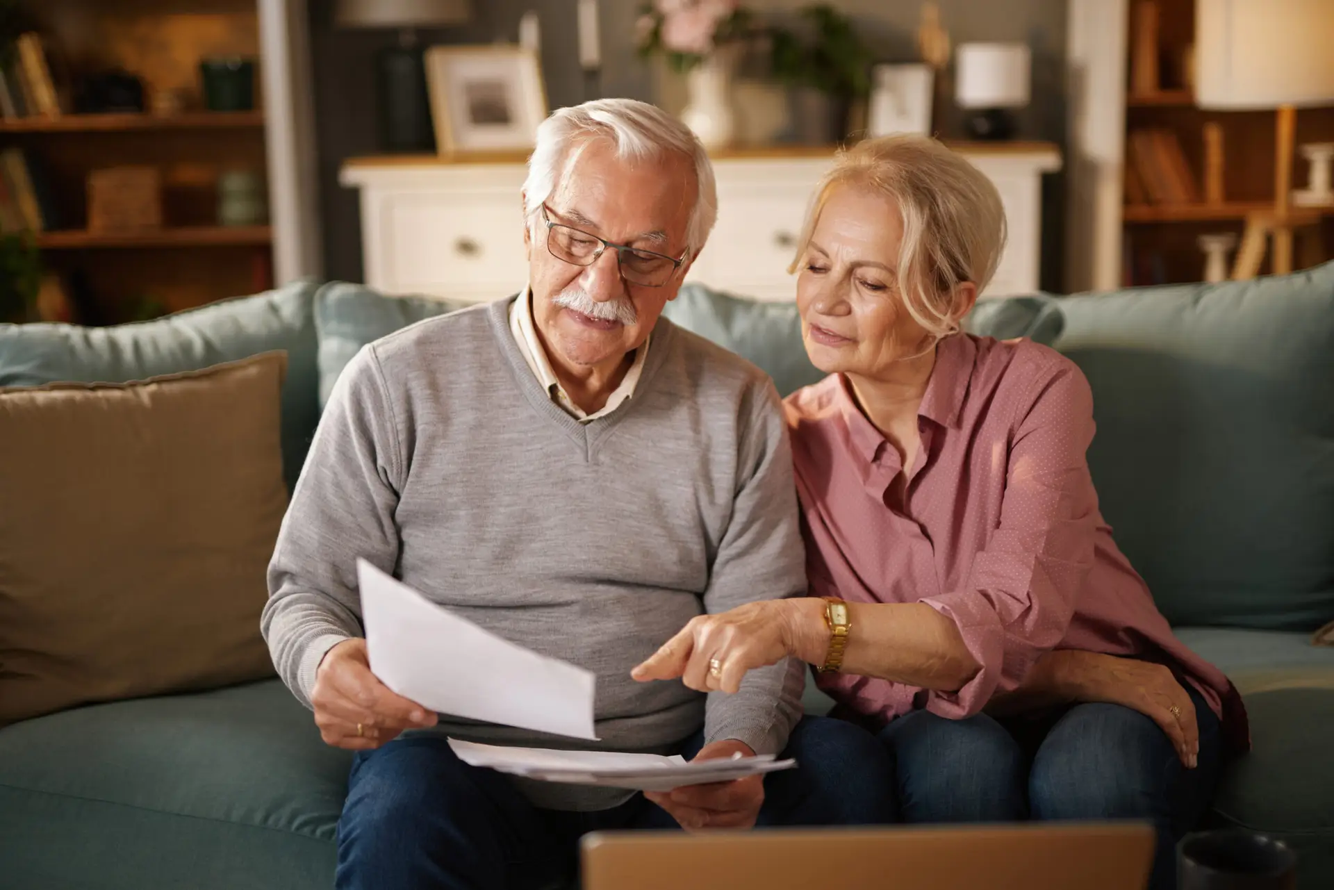 Senior couple reviewing life insurance documents on couch in living room, planning future finances and security together during a daytime meeting in their home