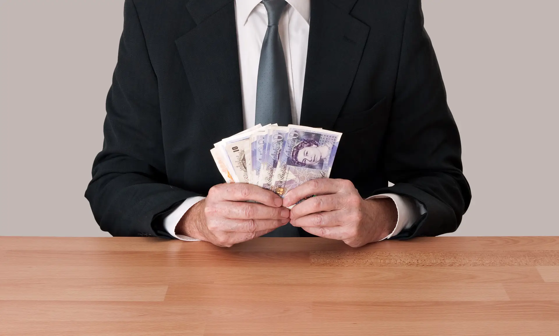 Man in suit sitting with cash - pounds sterling