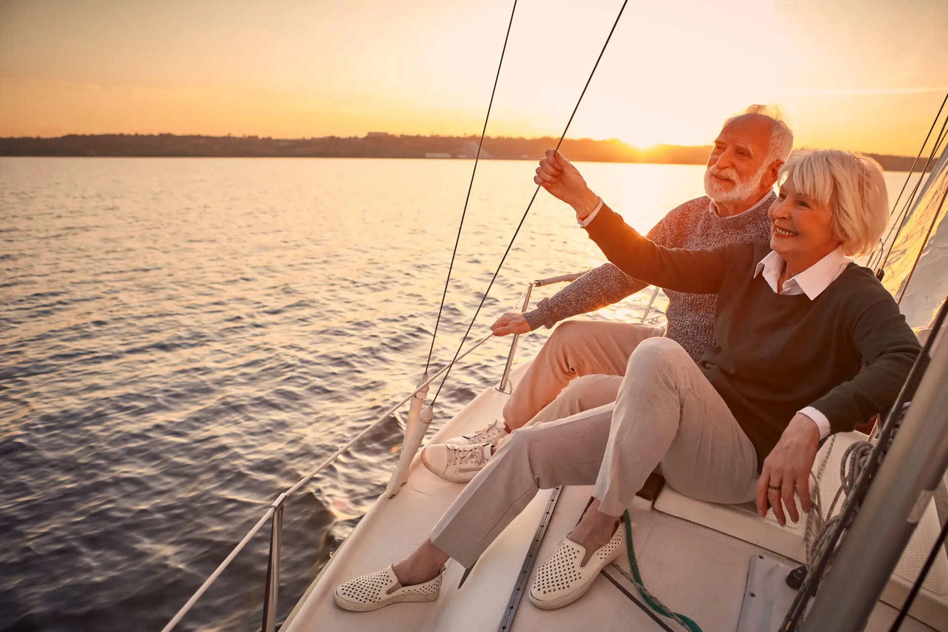 Enjoying luxury life. Beautiful happy senior couple in love relaxing on the side of sailboat or yacht deck floating in sea at sunset, looking at amazing evening view