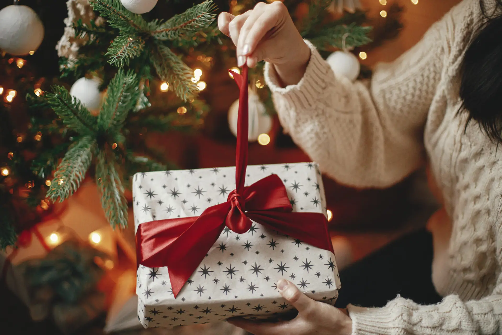 Hands in cozy sweater opening christmas gift with red bow on bac