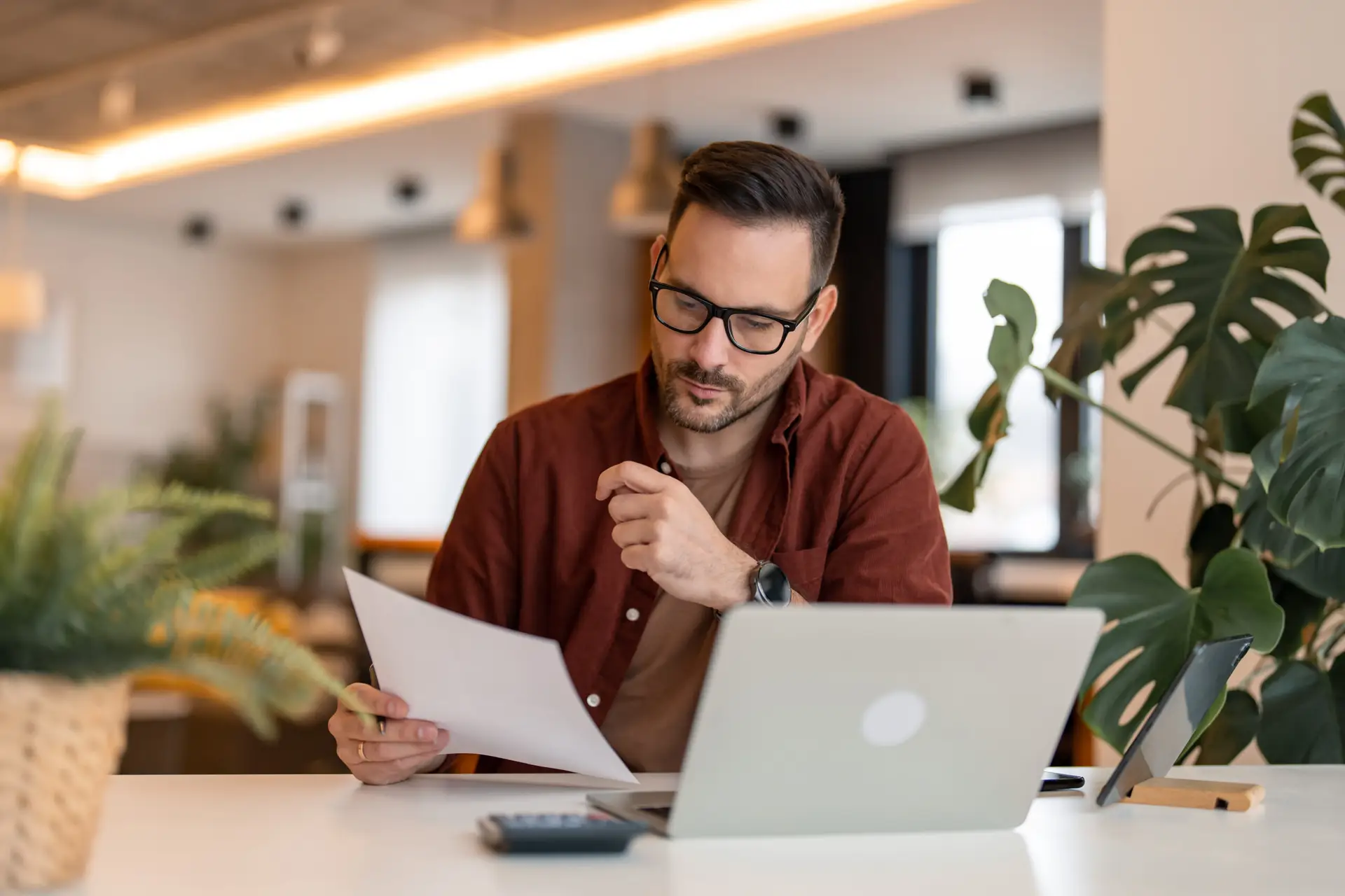 Serious millennial man using laptop sitting at the table in a ho