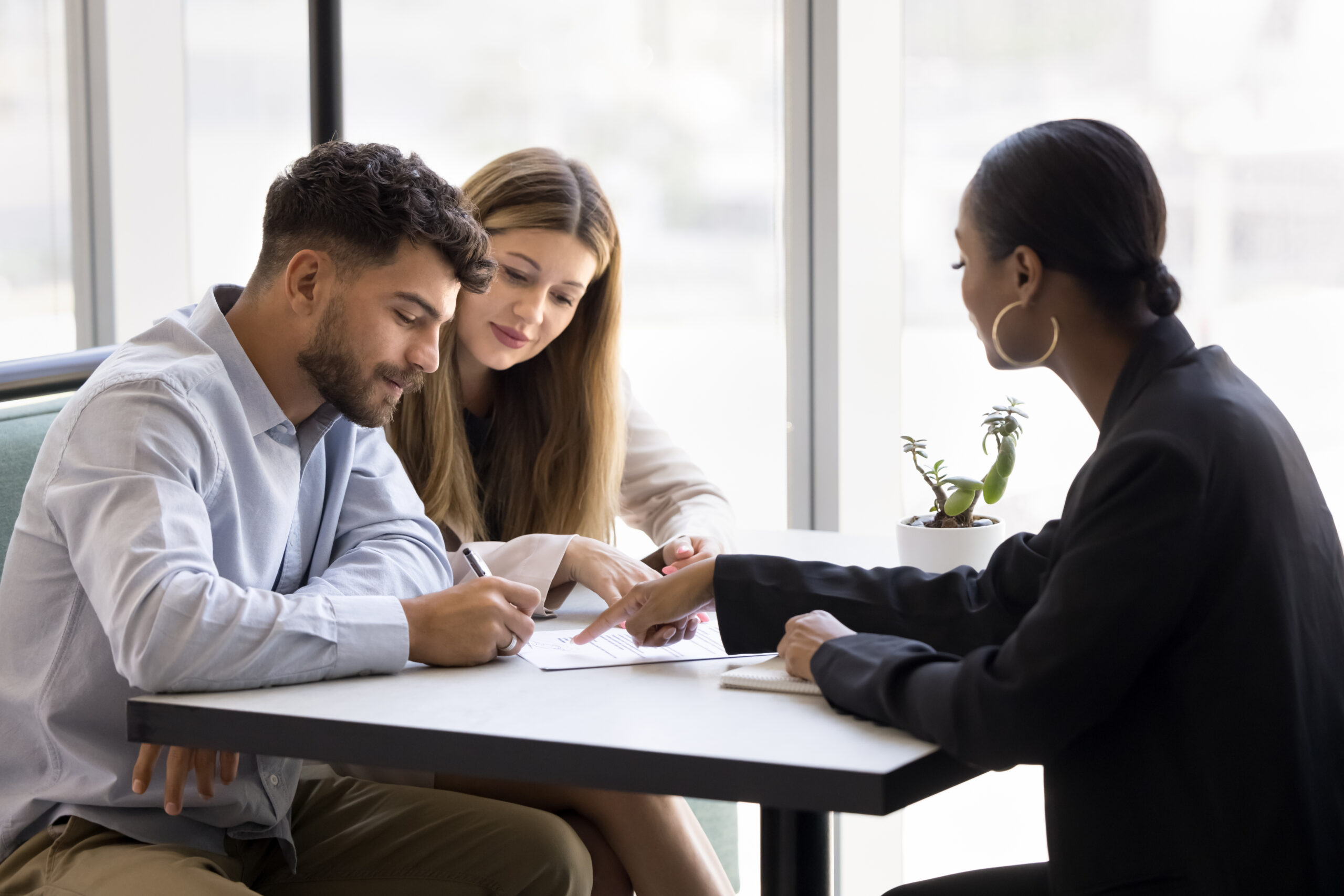 Confident young African realtor pointing at paper agreement for customers
