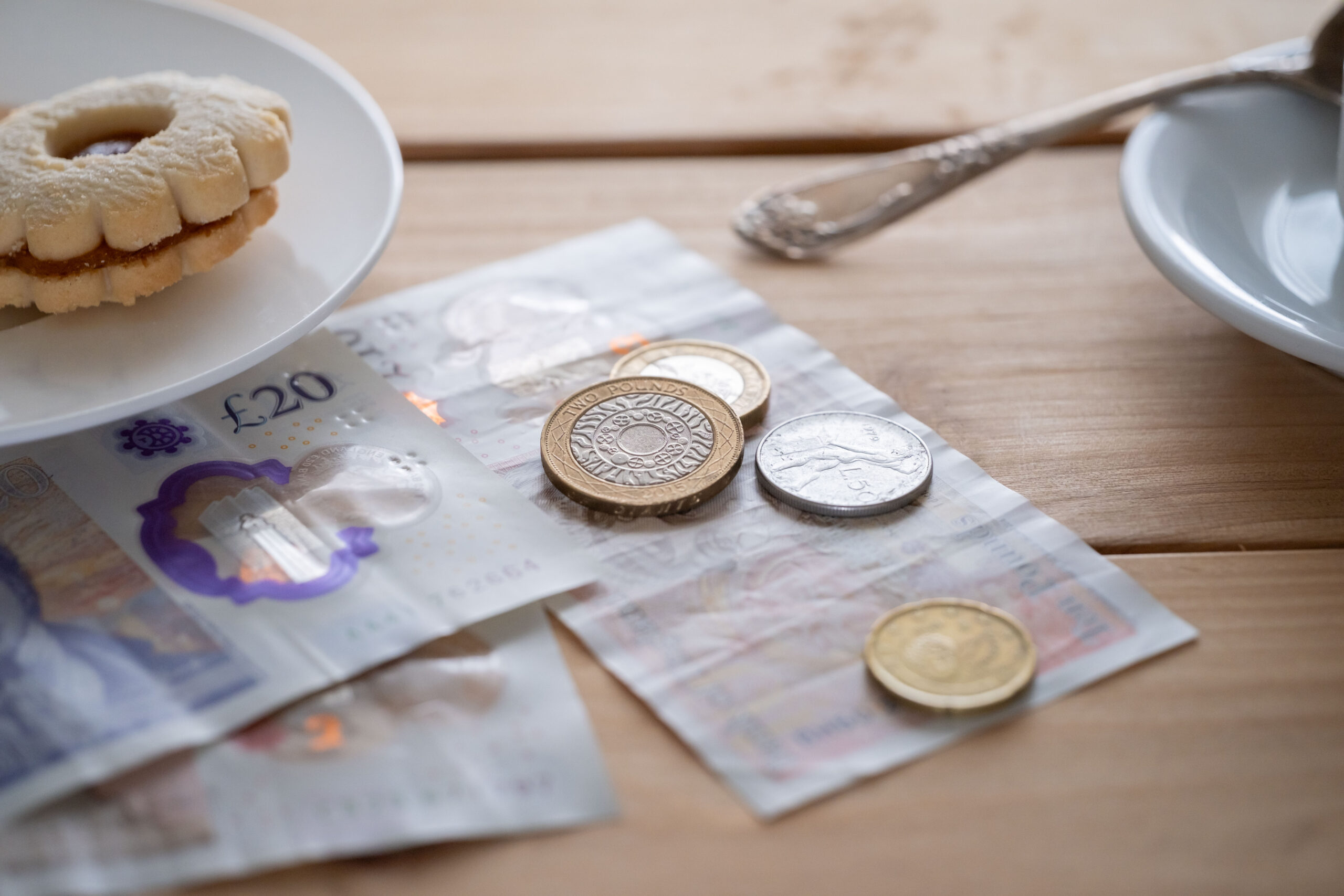 British pound sterling banknotes and coins on table with cookie and coffee cup nearby casual dining setting in cafe, UK pound currency beside snack, hospitality tipping, daily life, financial services