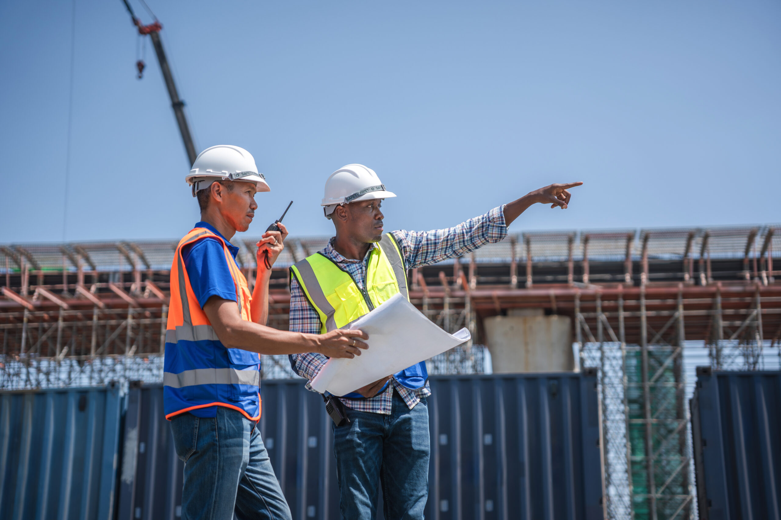 Diverse engineers discussing blueprints and pointing at construction site project, Professional foreman and engineer supervising industrial logistics and infrastructure building site