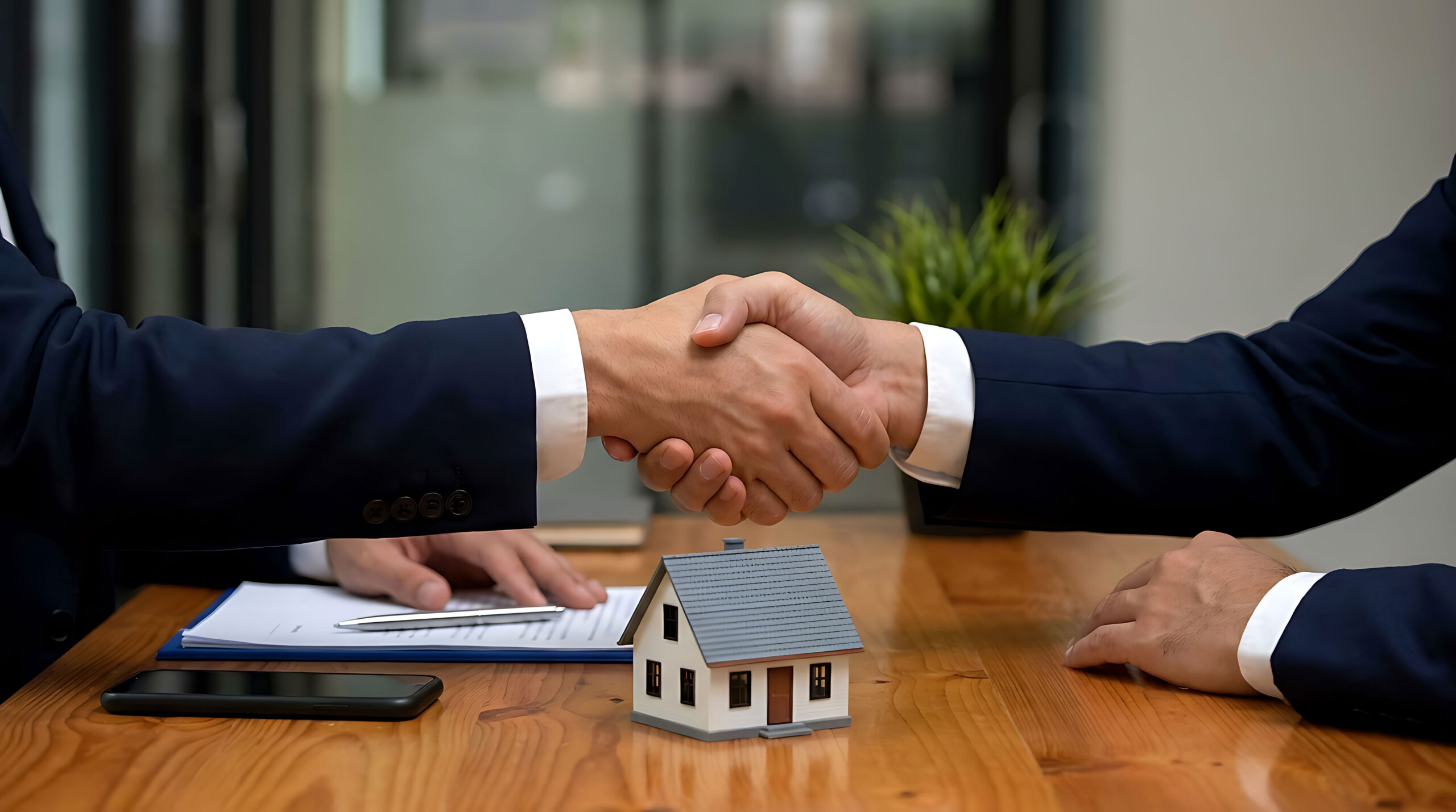 Real estate agents shaking hands over a house model in a professional office