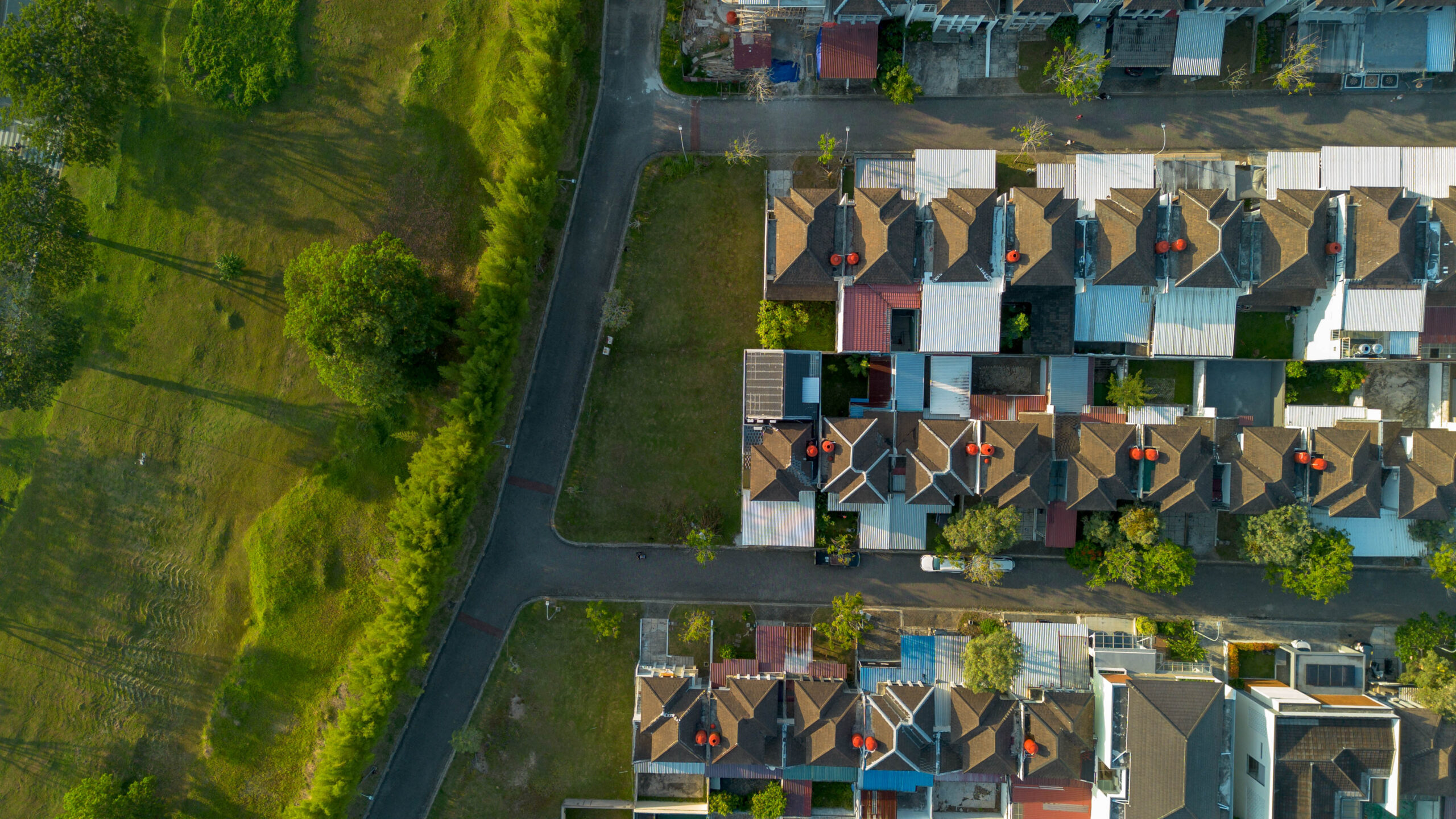 Top down aerial drone view of a modern suburban housing estate featuring uniform rows of houses with dark roofs and orange tanks adjacent to a large