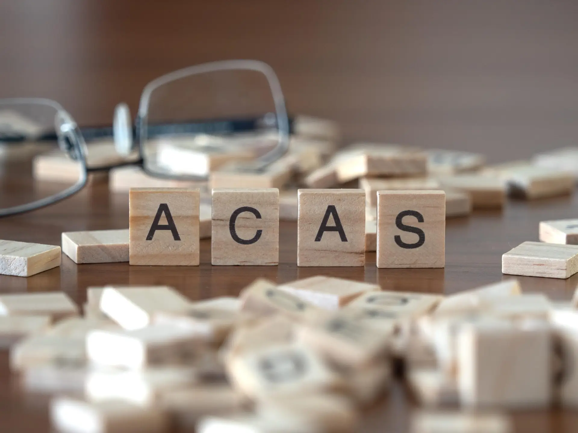 the acronym acas for advisory, conciliation and arbitration service word or concept represented by wooden letter tiles on a wooden table with glasses and a book